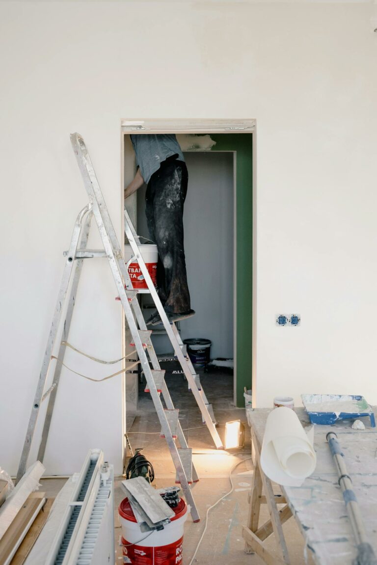 Indoor scene of home renovation with ladders, tools, and paint buckets.